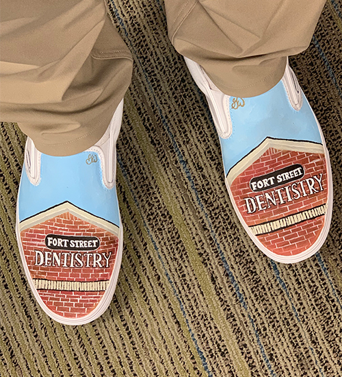 A person wearing blue shoes with a unique design featuring a brick wall, text, and an image of a building, all with a playful vibe.